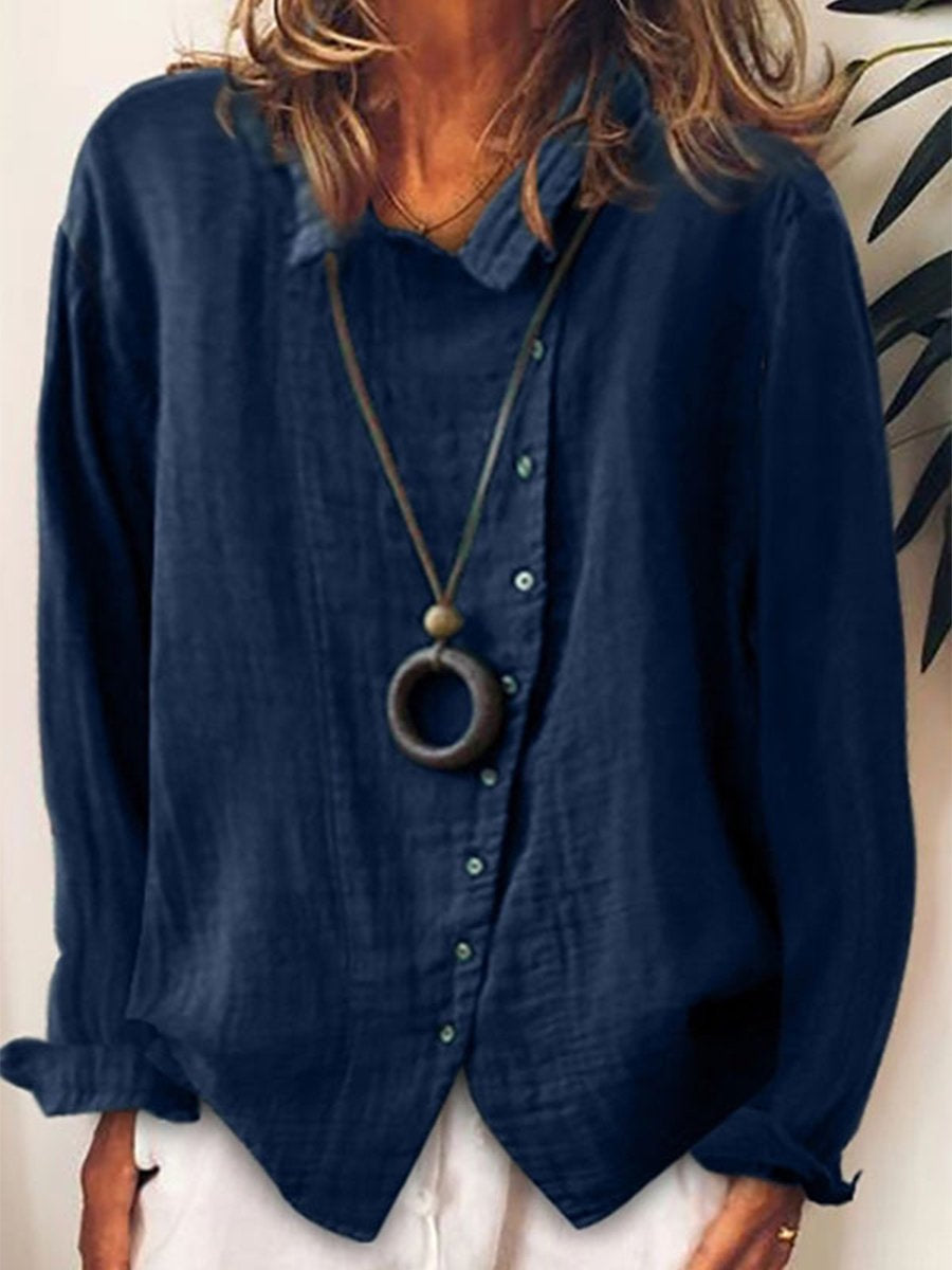 Femme portant une chemise bleu marine en lin avec col boutonné, manches longues et collier pendentif circulaire, style décontracté chic.