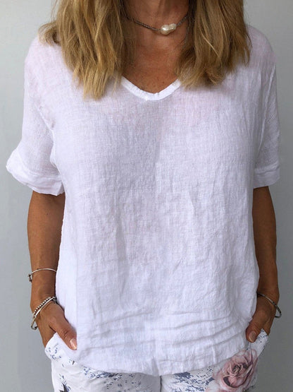 Femme portant un t-shirt en lin blanc, manches courtes, col en V, avec un collier perle. Mode estivale décontractée, tendance et élégante.