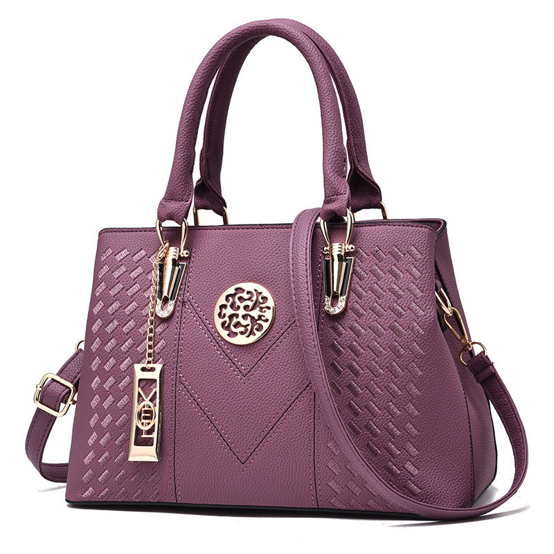 Lila Damenhandtasche aus Leder mit geprägtem Muster und goldenen Details, elegant und modisch.