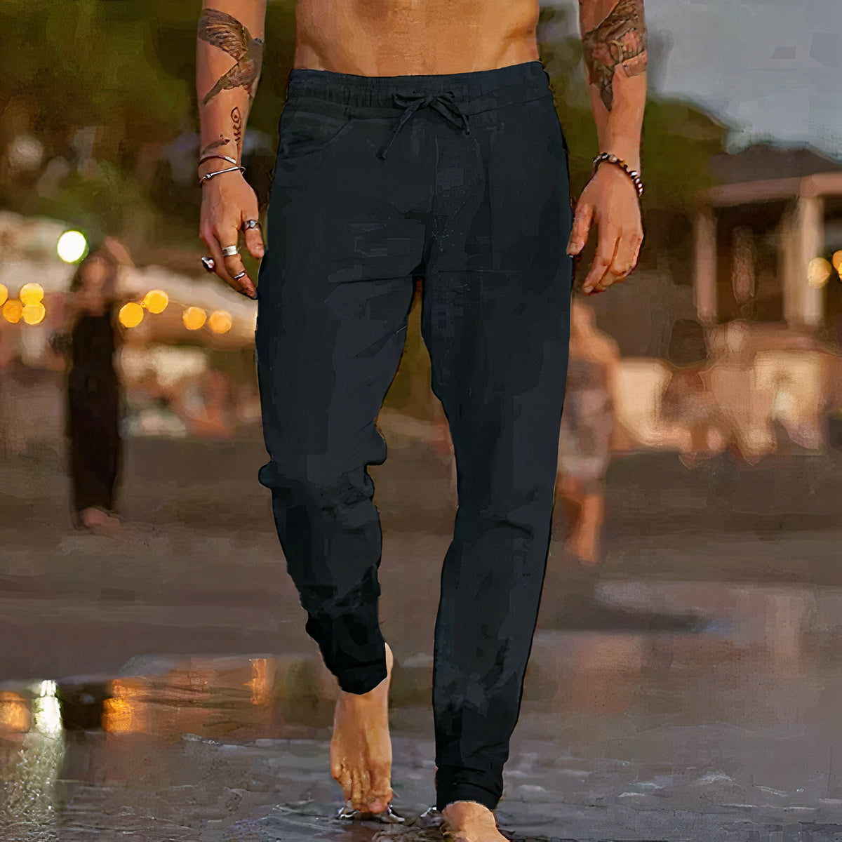 Homme torse nu portant un pantalon de jogging noir sur la plage au coucher du soleil, ambiance décontractée, mode masculine, style estival.