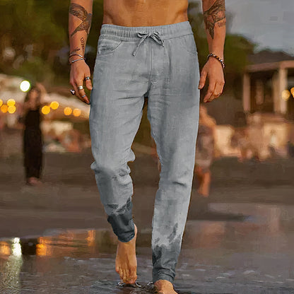 Homme marchant sur la plage au coucher du soleil, portant un pantalon de jogging gris mouillé. Scène estivale, ambiance décontractée, bord de mer.