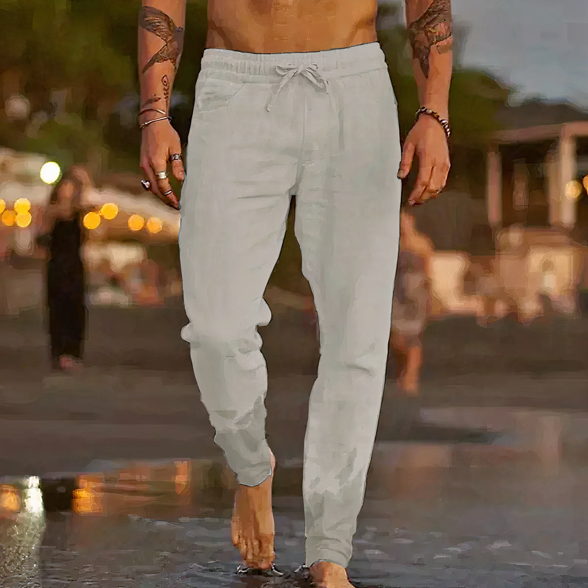 Homme torse nu marchant sur la plage au coucher du soleil, portant un pantalon de jogging gris clair, ambiance estivale et décontractée.
