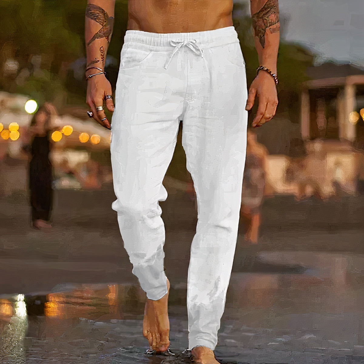 Homme marchant sur la plage au coucher du soleil, portant un pantalon blanc en lin, pieds nus. Mode estivale décontractée, ambiance bord de mer.