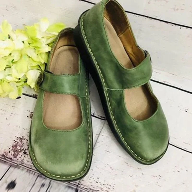 Chaussures vertes en cuir pour femmes avec bride, posées sur un sol en bois clair, accompagnées de fleurs blanches. Mode, confort, style vintage.