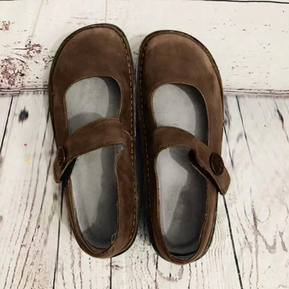 Chaussures Mary Jane marron en daim sur fond en bois clair, style vintage, confortables et élégantes, idéales pour un look rétro chic.