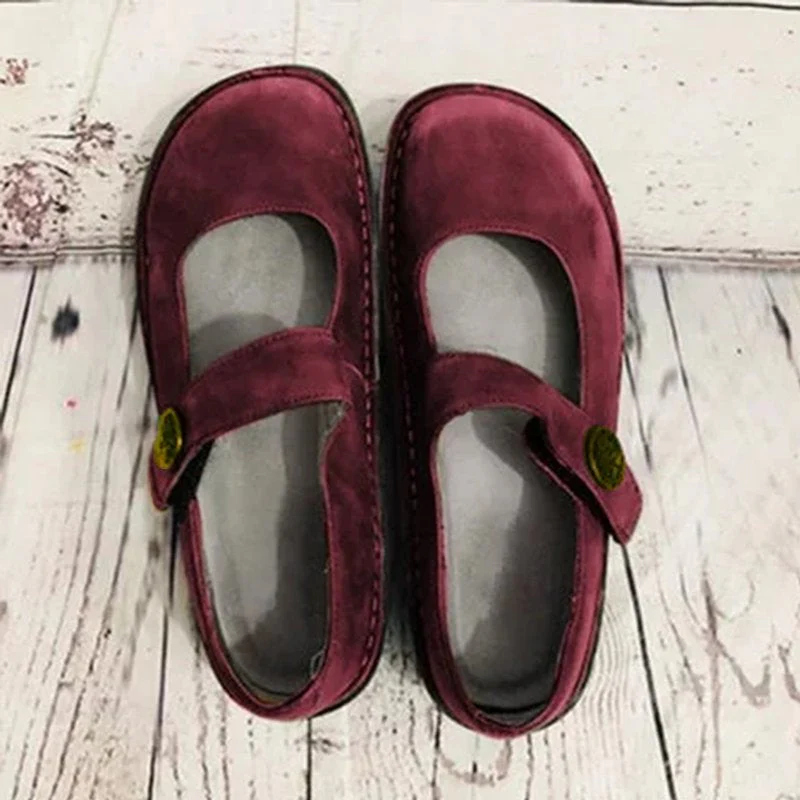 Chaussures Mary Jane en daim bordeaux sur plancher en bois clair, style vintage, boucle dorée, confort et élégance pour femmes.