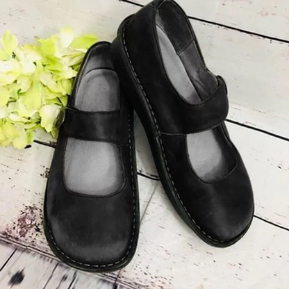 Chaussures Mary Jane noires en cuir sur fond en bois, avec fleurs vertes. Chaussures élégantes pour femmes, style classique et confortable.