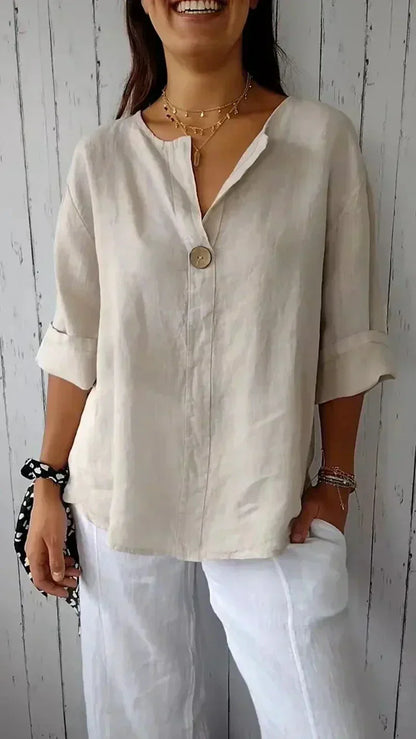 Femme portant une chemise en lin beige avec un bouton, manches retroussées, et un pantalon blanc. Style décontracté, mode estivale, élégance simple.