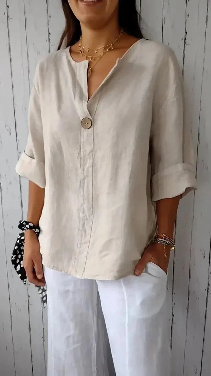 Femme portant une chemise en lin beige avec bouton, manches retroussées, associée à un pantalon blanc. Style décontracté, mode estivale élégante.