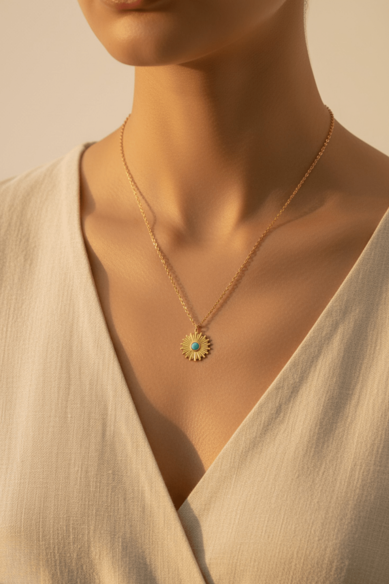 Vrouw draagt de Monerose Soleil Ketting Turquoise Zon variant op een beige linnen outfit, gouden zonnehanger met turquoise steen zichtbaar op decolleté, 18K goldplated 316L roestvrij staal, Lumière collectie van Monerose