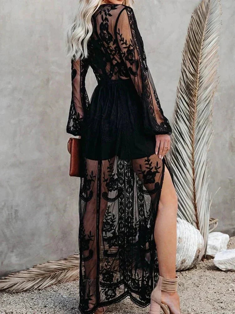 Robe longue noire en dentelle transparente avec motifs floraux, manches longues, fendue, portée par une femme blonde, style élégant et chic.