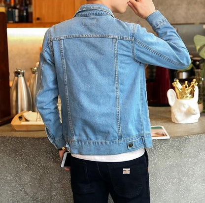 Homme en veste en jean bleu, de dos, tenant un smartphone, dans un café moderne. Mode décontractée, style urbain, ambiance détendue.