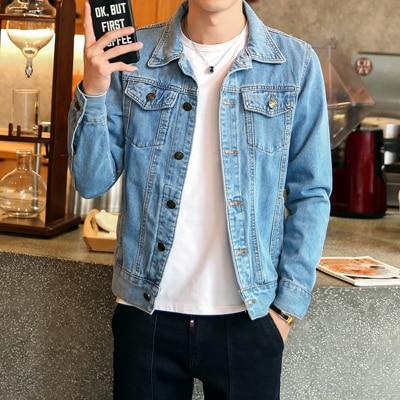 Homme portant une veste en jean bleu, tenant un smartphone dans un café moderne. Mode décontractée, style urbain, tendance vestimentaire masculine.
