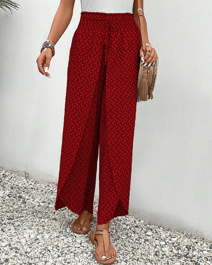 Pantalon large rouge à motifs géométriques, porté avec un haut blanc et des sandales marron. Style décontracté estival pour femme.