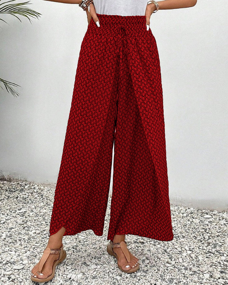 Pantalon large rouge à motifs géométriques, porté avec des sandales beiges sur fond de gravier. Mode féminine, style décontracté, tendance été.