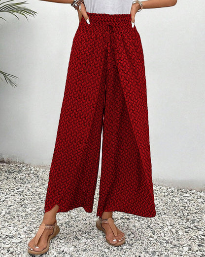 Pantalon large rouge à motifs géométriques, porté avec des sandales beiges sur fond de gravier. Mode féminine, style décontracté, tendance été.