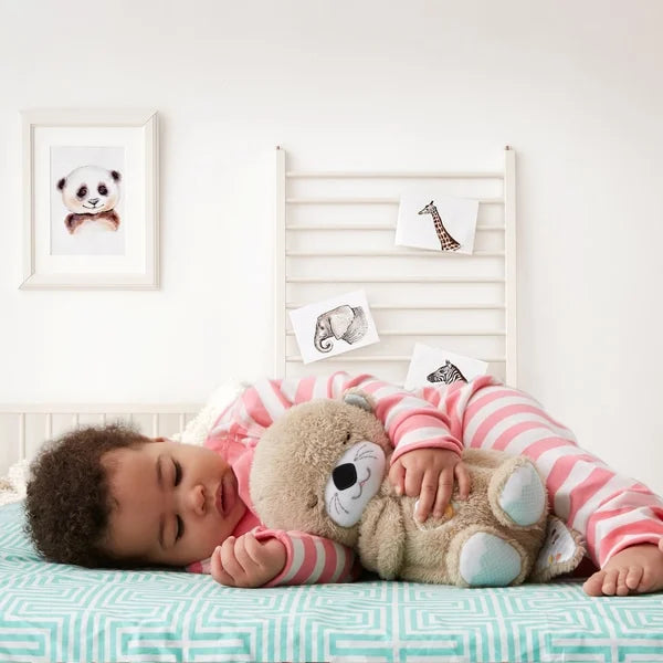 Kleinkind schläft mit Fisher-Price Plüschbär, rosa gestreifter Schlafanzug, Kinderzimmer.