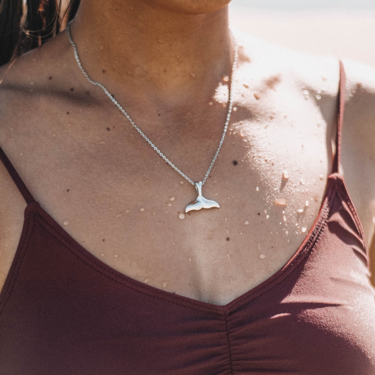 Frau mit silberner Walflossen-Halskette, Strand, Sommermode, Schmuck, Damenaccessoire.