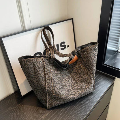 Sac à main en toile imprimé léopard, posé sur une table noire, avec un cadre minimaliste en arrière-plan. Mode, accessoire tendance, design chic.