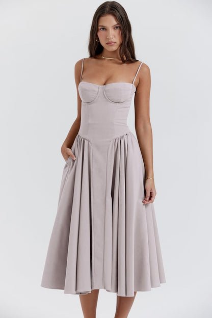 Robe midi élégante beige avec bretelles fines, corsage ajusté et jupe évasée, portée par une femme sur fond blanc. Mode féminine chic.
