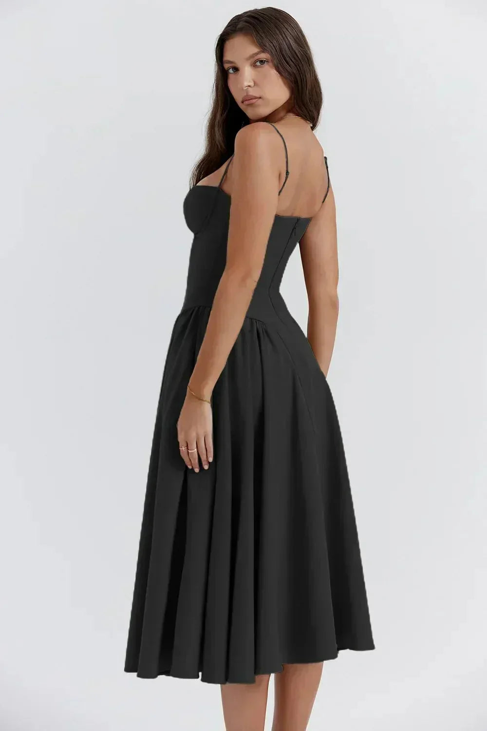 Femme portant une robe noire élégante, dos nu, longueur mi-mollet, bretelles fines, style chic et moderne, sur fond blanc. Mode féminine tendance.